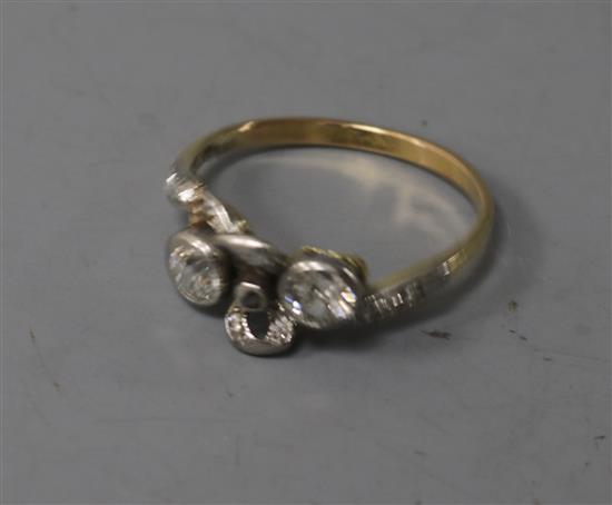 An early 20th century yellow metal and two stone diamond ribbon bow crossover ring, size M.